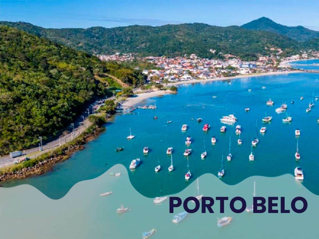 Vista aérea de Porto Belo, Santa Catarina, com barcos na água e montanhas ao fundo. Porto Belo.