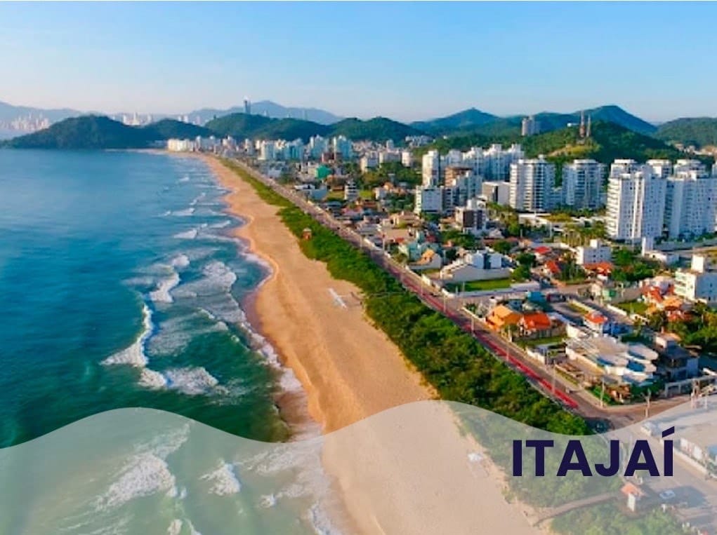Vista panorâmica da praia de Itajaí, Santa Catarina, com prédios e montanhas ao fundo.