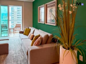 Sala de estar moderna com sofá cinza, parede verde e varanda com vista da cidade. Decoração de "Royal Summer".