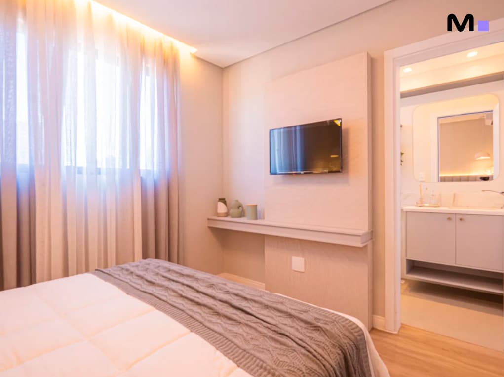 Quarto moderno com TV no Edifício Leblon Residence. Cama confortável, janela iluminada e banheiro integrado.