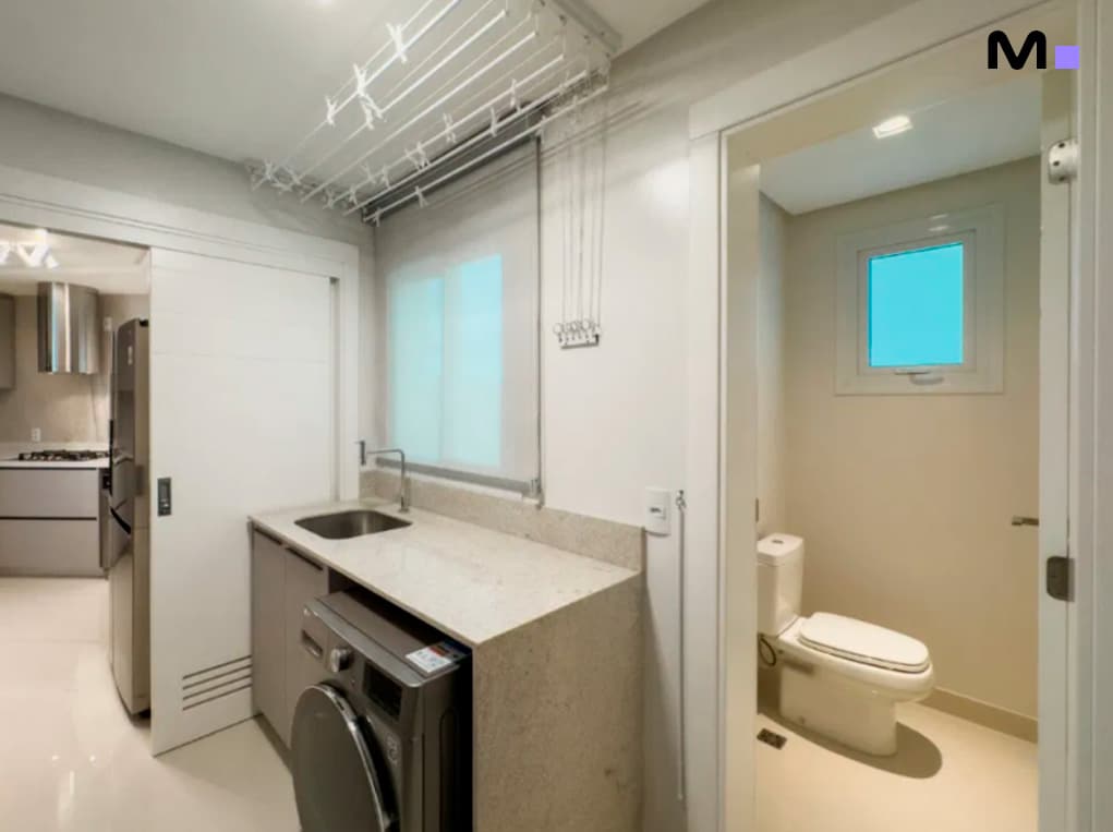 Lavanderia moderna com máquina de lavar e acesso ao banheiro na Infinity Coast Residence.