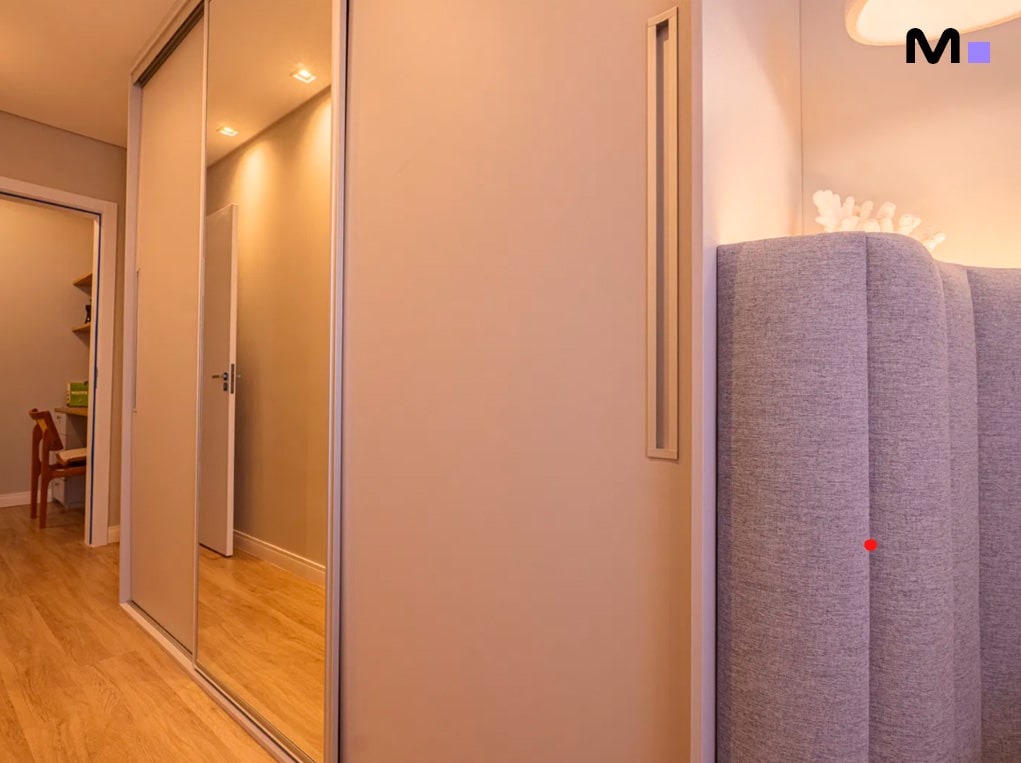 Armário espelhado no Edifício Leblon Residence, refletindo um corredor com piso de madeira e porta aberta.