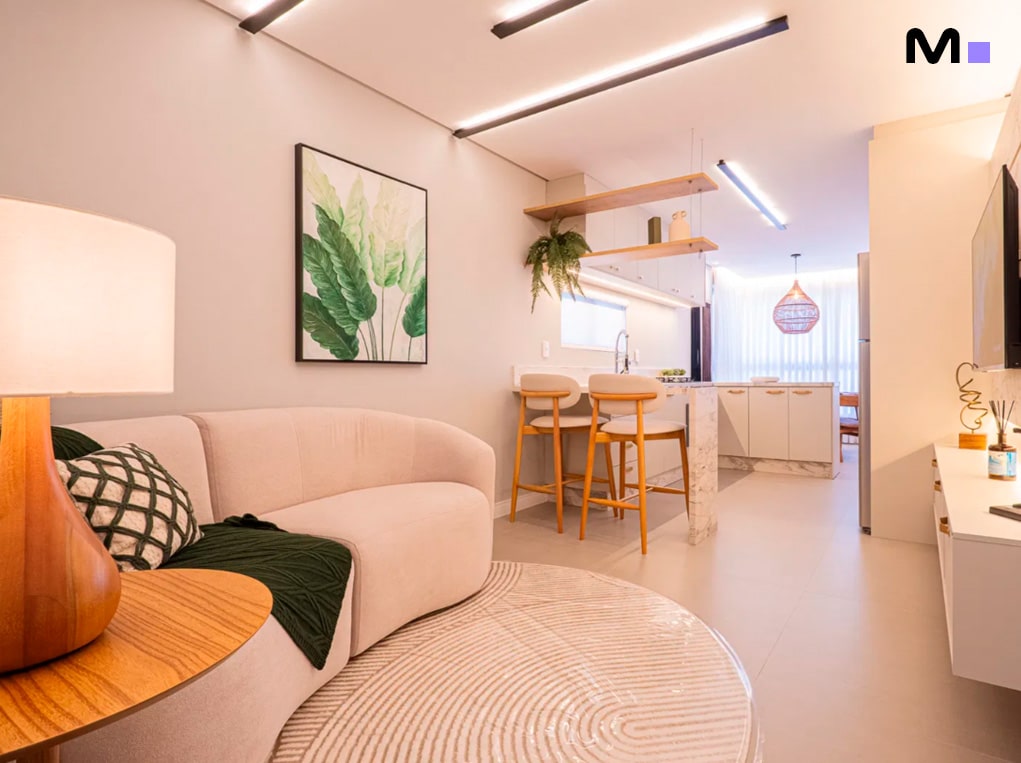 Sala de estar moderna com sofá curvo, arte de parede botânica e cozinha aberta no Edifício Leblon Residence.