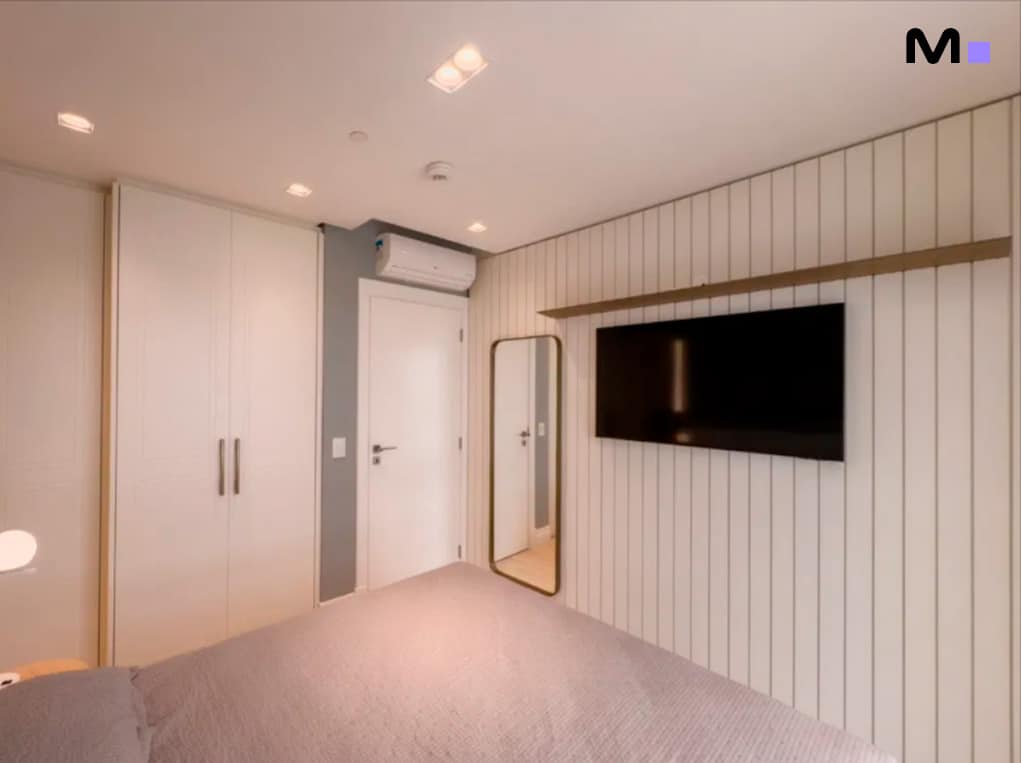 Quarto moderno com TV, guarda-roupa branco e espelho. Design de interiores da Infinity Coast Residence.