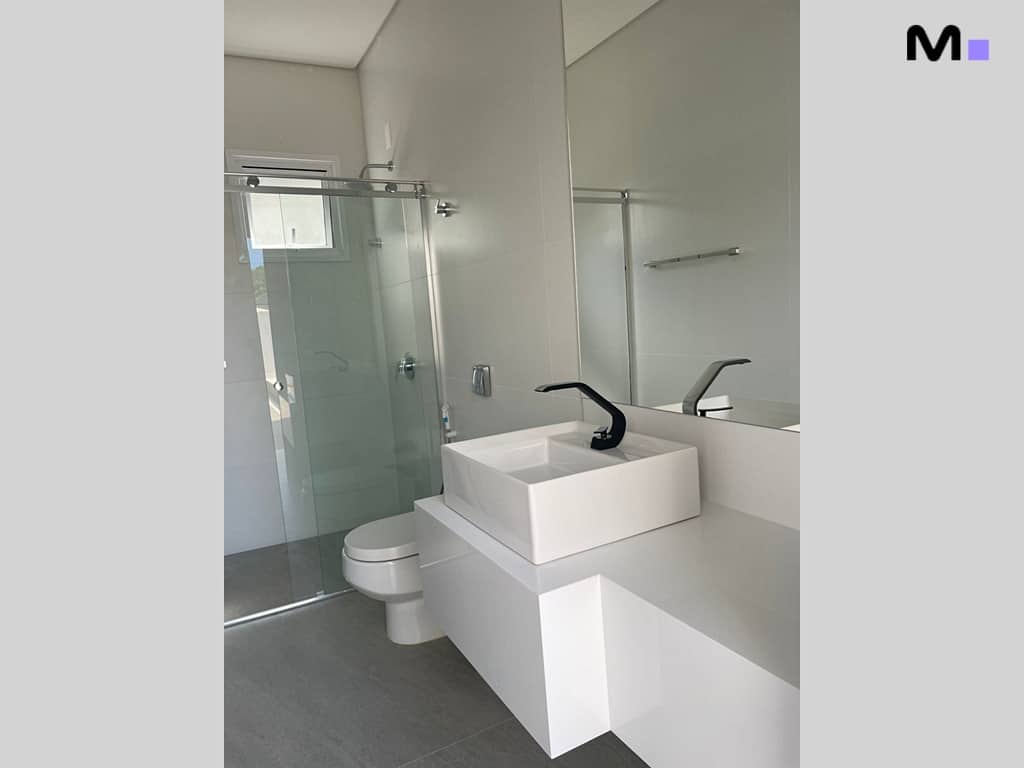 Banheiro moderno e minimalista com pia branca, torneira preta e box de vidro. Condomínio House Haras.