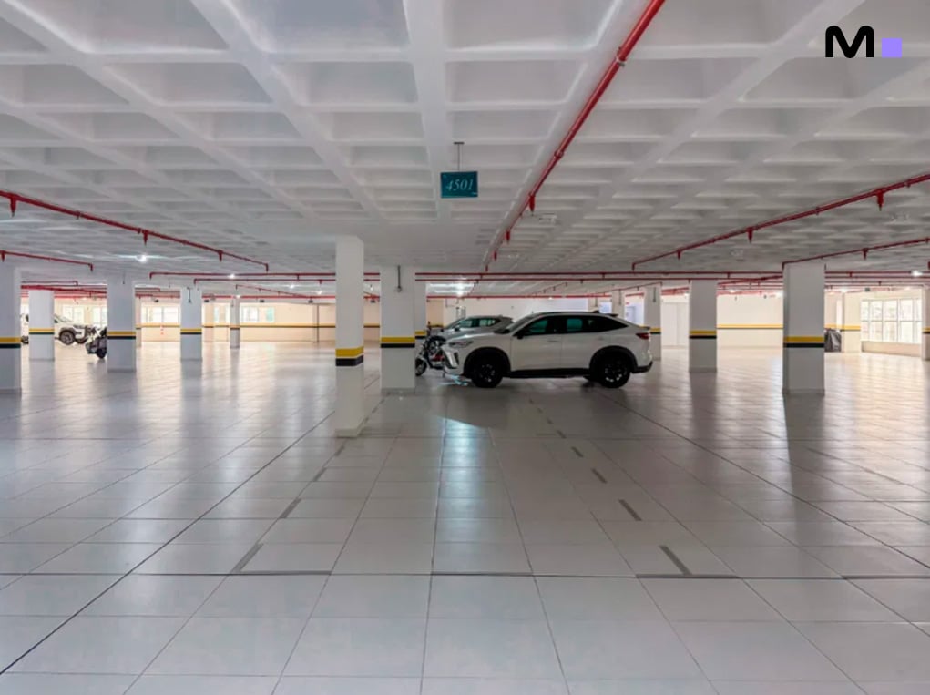 Estacionamento espaçoso no Infinity Coast Residence com carro branco e colunas marcadas em amarelo e preto.