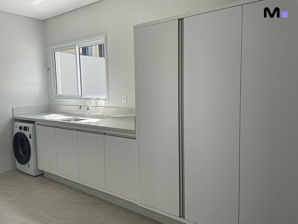 Lavanderia moderna e minimalista com máquina de lavar, pia e armários brancos no Condomínio House Haras.