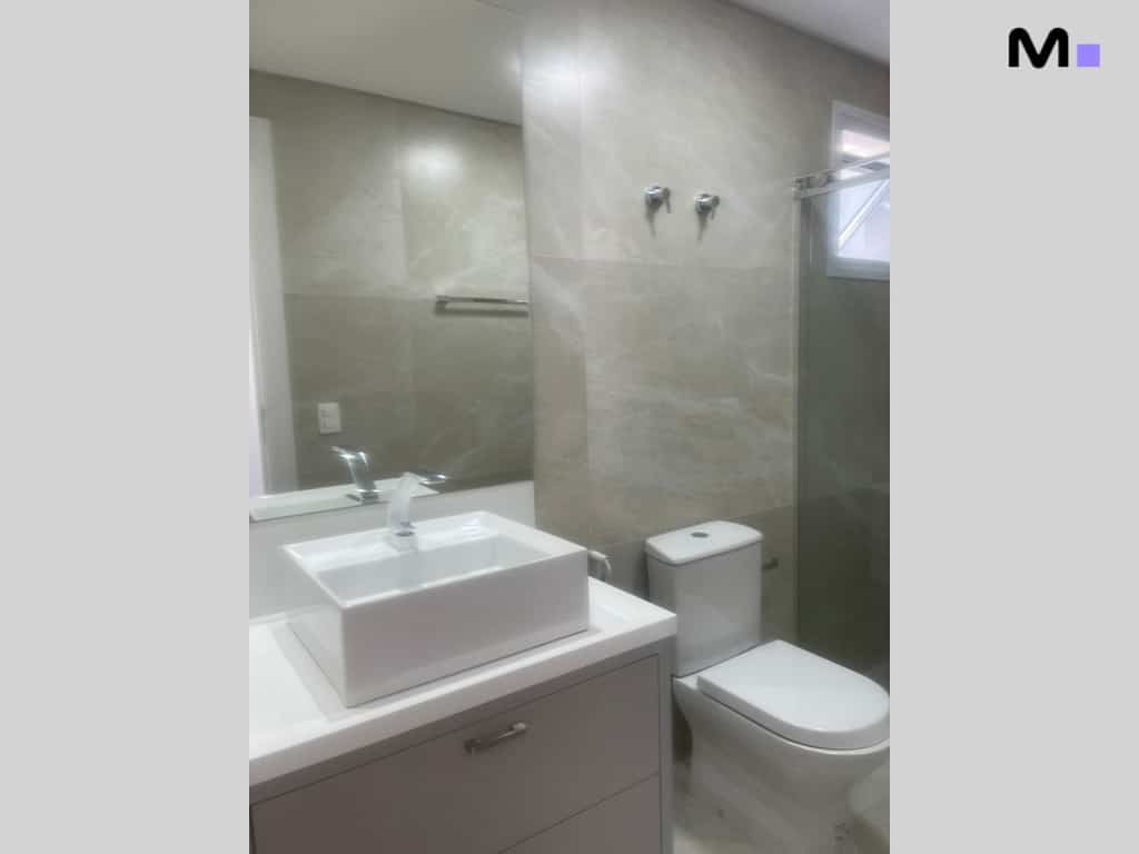 Banheiro moderno com pia branca, espelho grande e vaso sanitário. Condomínio House Haras.