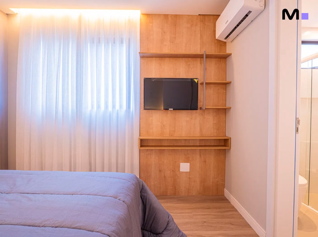 Quarto moderno com cama, TV embutida e cortinas claras no Edifício Leblon Residence.