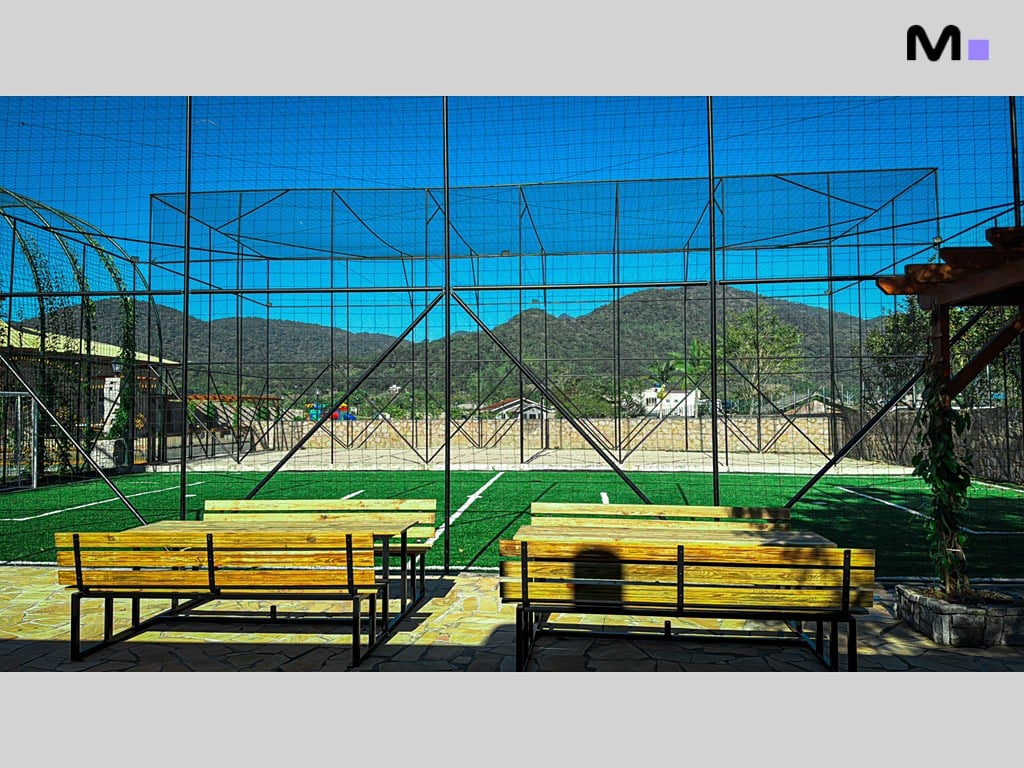 Mesas no Condomínio Vale das Pedras em área de lazer com gramado e rede de proteção.