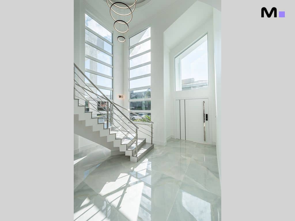 Hall de entrada luxuoso com escada moderna e piso de mármore refletindo a luz.