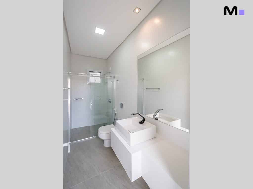 Banheiro moderno e clean com pia branca e box de vidro.