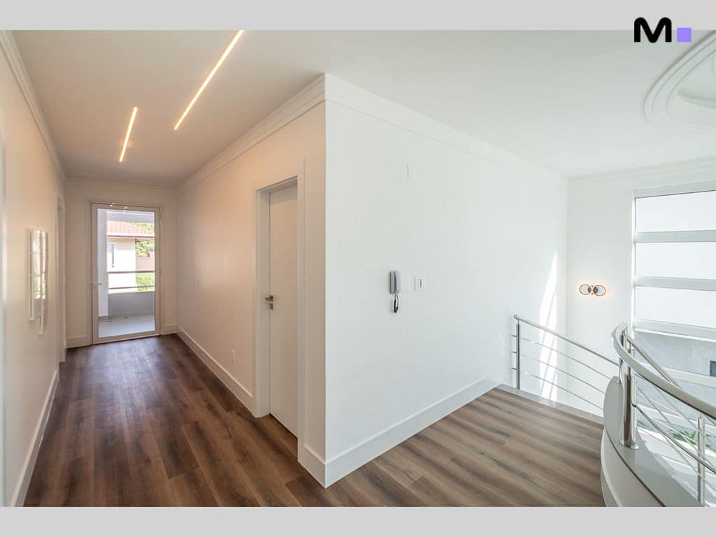 Corredor moderno e iluminado no Condomínio House Haras, com piso de madeira e detalhes em branco.