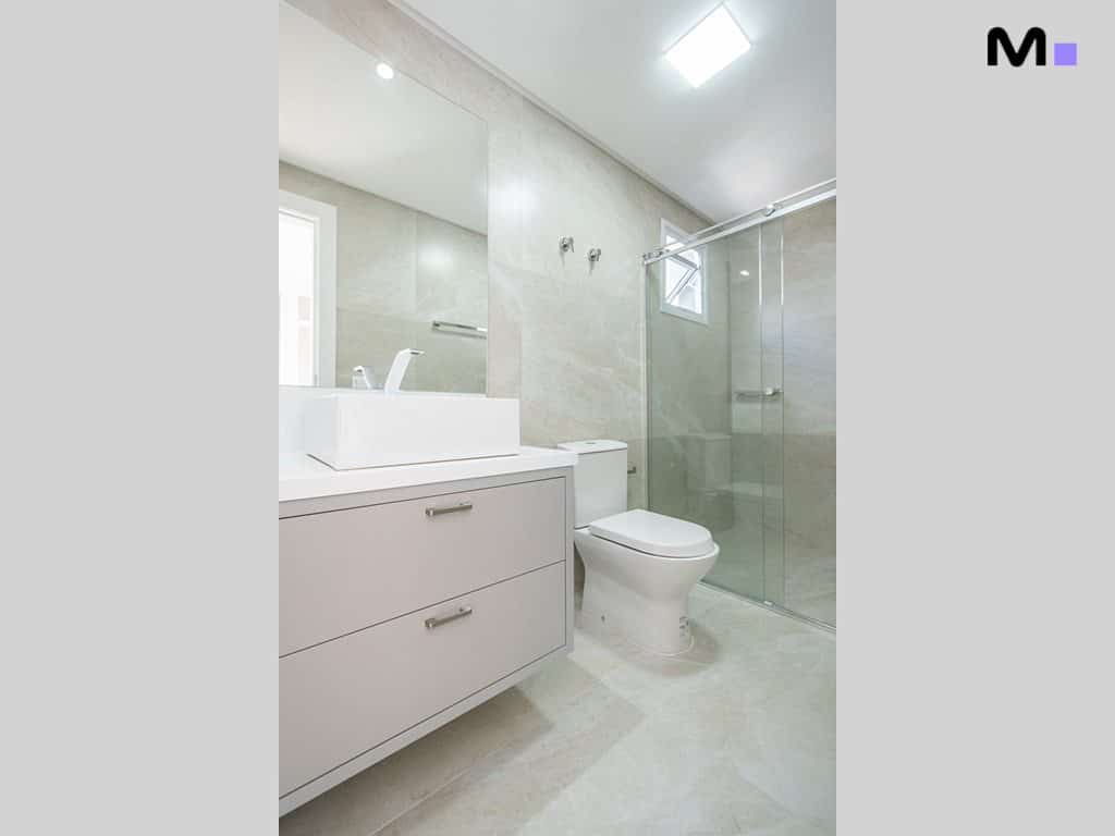 Banheiro moderno com pia branca, espelho grande e box de vidro no Condomínio House Haras.