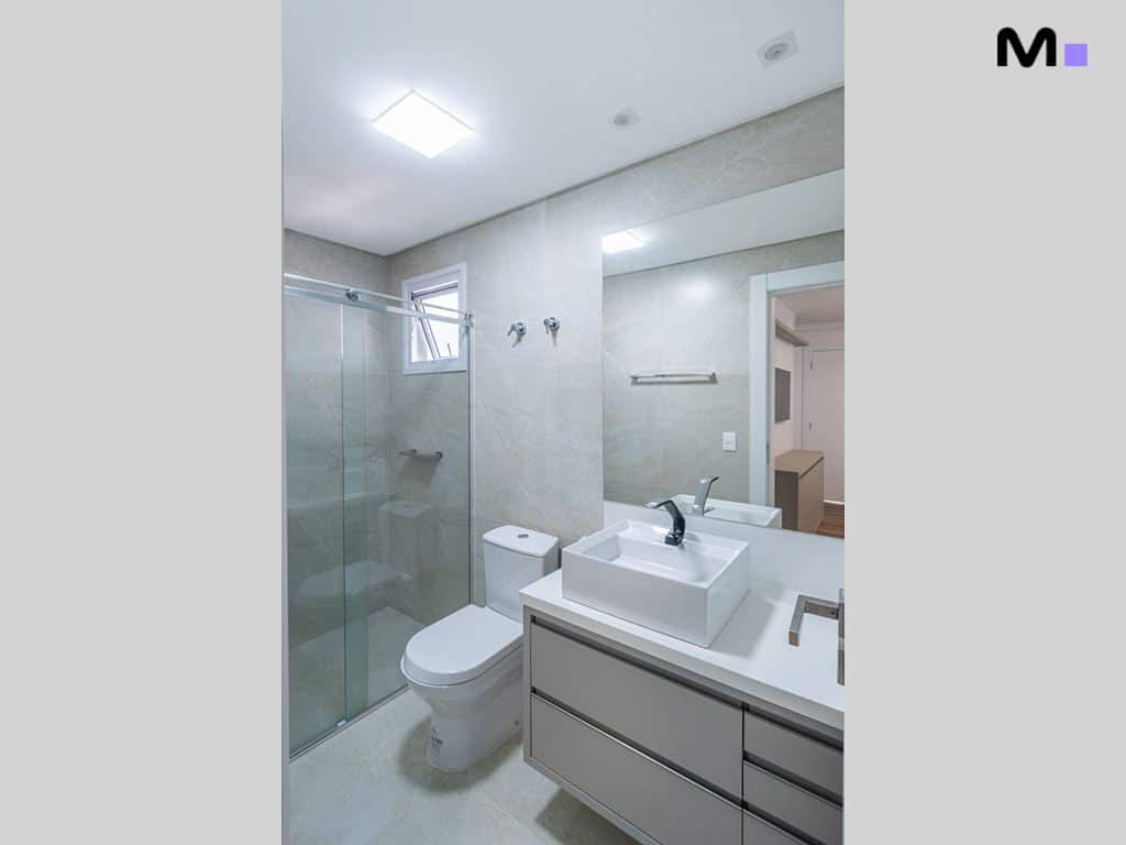 Banheiro moderno com pia branca, vaso sanitário e box de vidro no Condomínio House Haras.