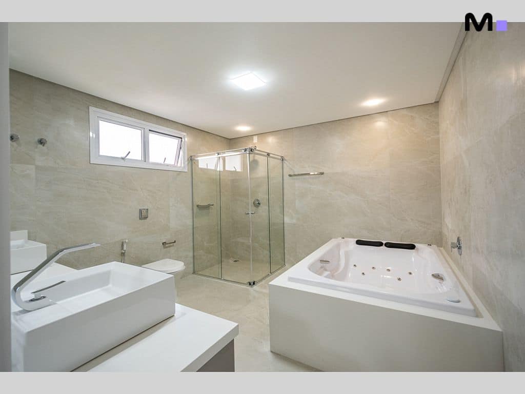 Banheiro moderno com banheira de hidromassagem, chuveiro de vidro e pia branca. Condomínio House Haras.