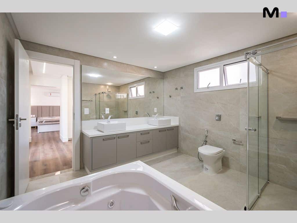 Banheiro moderno e iluminado no Condomínio House Haras, com banheira, pia dupla e box de vidro.