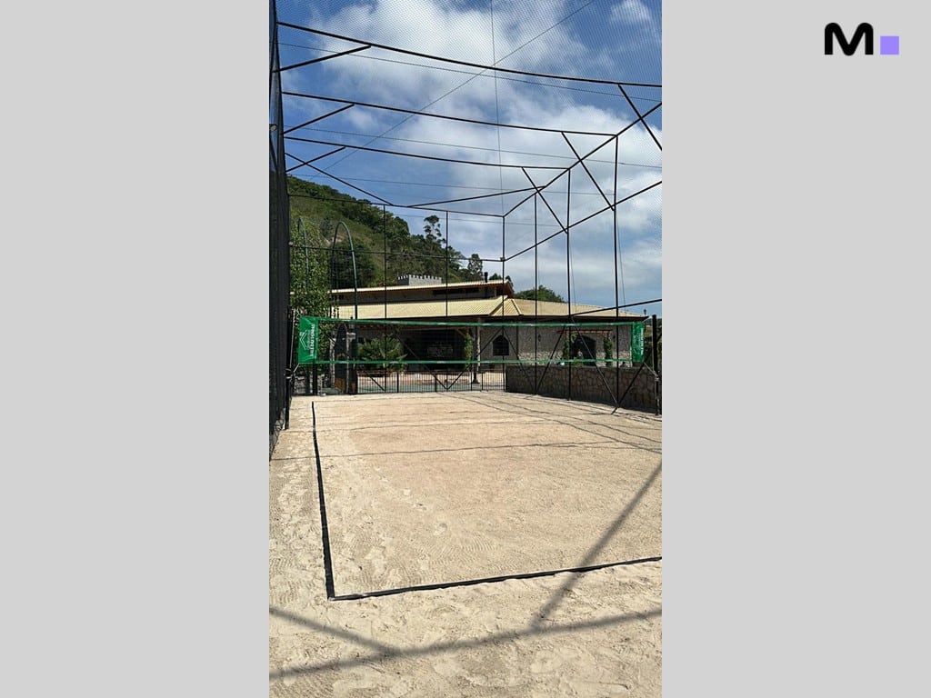 Quadra de areia para beach tennis no Condomínio Vale das Pedras. Rede verde e céu azul.