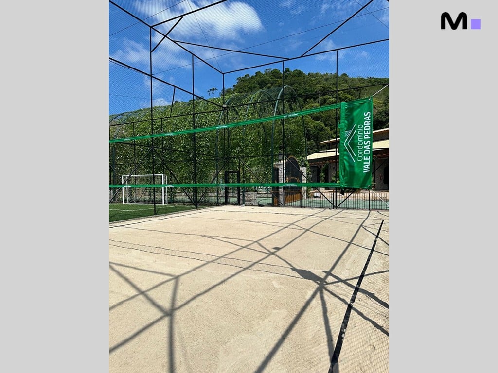 Quadra esportiva do Condomínio Vale das Pedras com rede e gramado ao fundo.