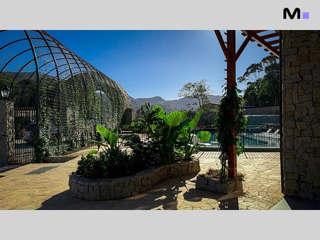 Paisagem do Condomínio Vale das Pedras com piscina, vegetação e arquitetura em pedra.