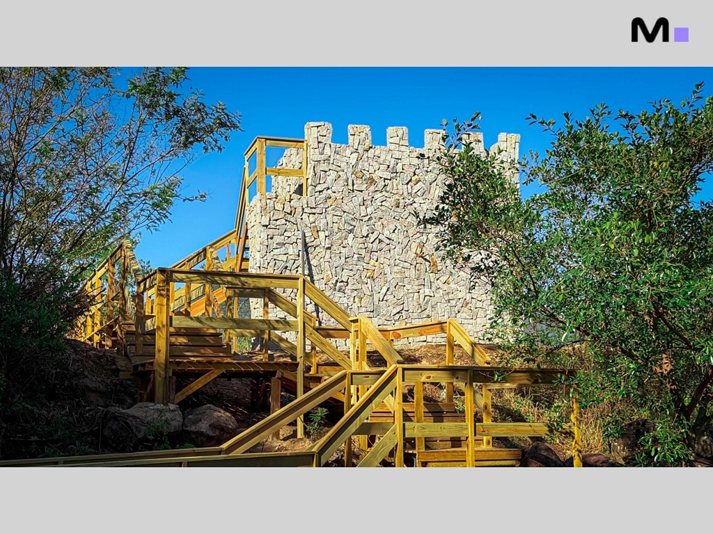 Escadaria de madeira rústica levando a uma torre de pedra no Condomínio Vale das Pedras.