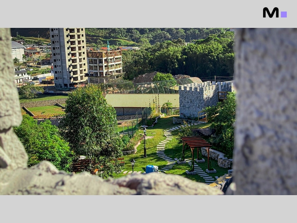 Vista do Condomínio Vale das Pedras, com área verde, torre e construções ao fundo.
