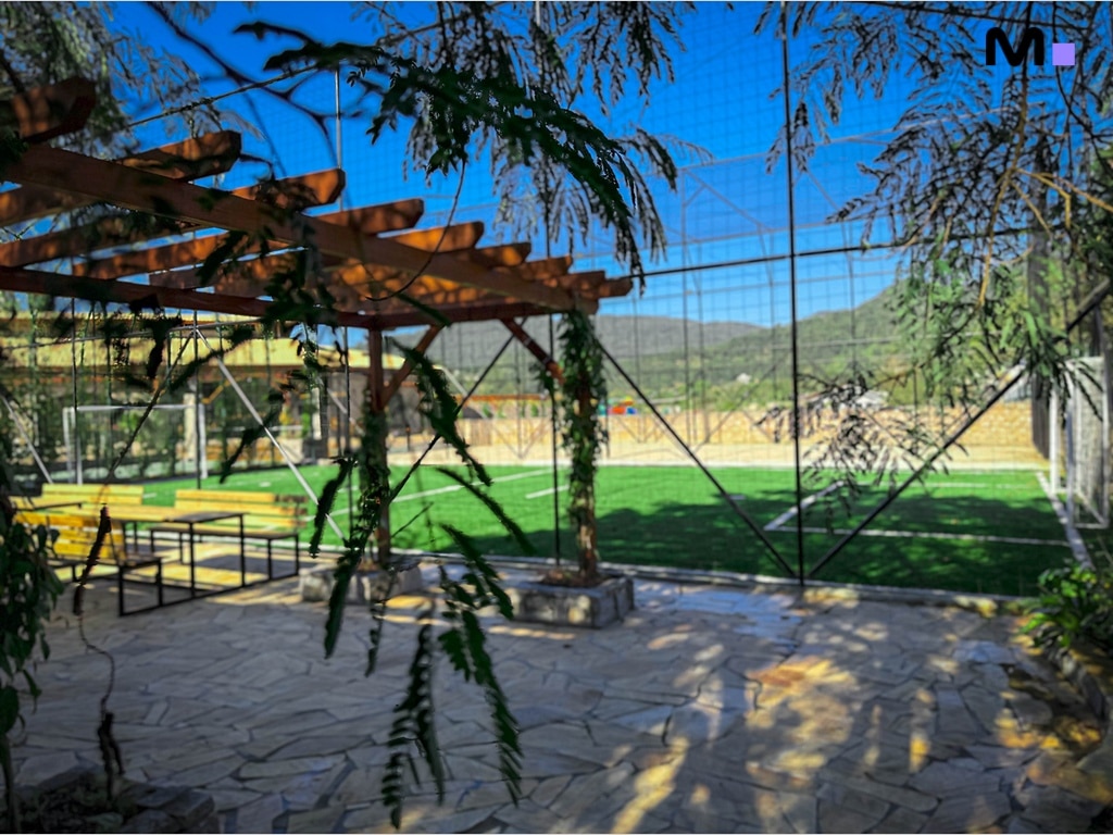 Campo de futebol no Condomínio Vale das Pedras, com área de lazer e montanhas ao fundo.