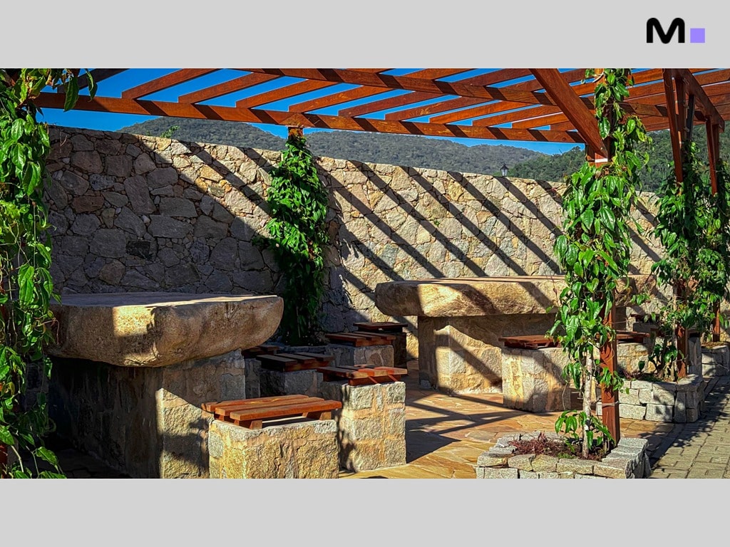 Área de lazer com pergolado e bancos de pedra no Condomínio Vale das Pedras.