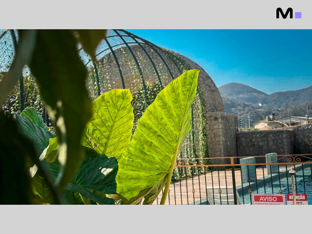Vista do Condomínio Vale das Pedras com vegetação exuberante e piscina. Aviso: Atenção.