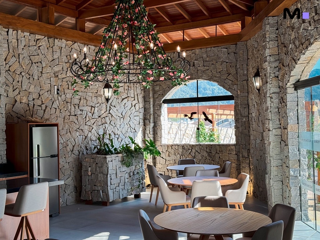 Interior rústico e elegante do Condomínio Vale das Pedras com mesas, cadeiras e decoração em pedra.