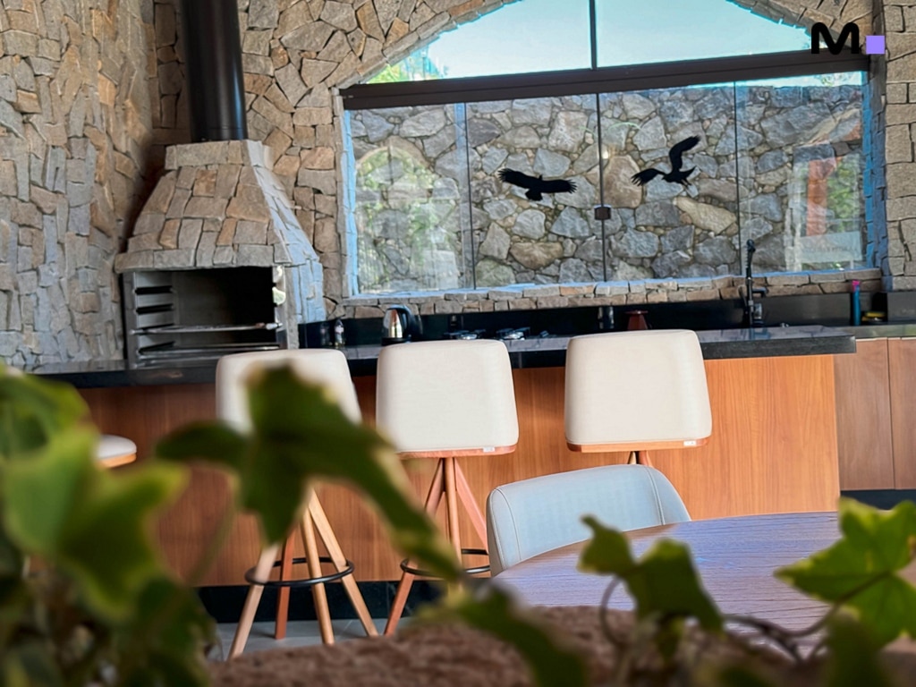 Interior moderno com balcão, cadeiras e lareira de pedra no Condomínio Vale das Pedras.