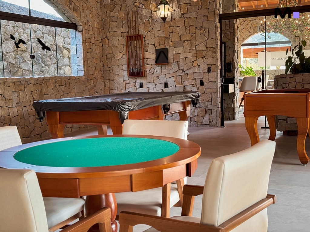 Sala de jogos no Condomínio Vale das Pedras com mesa de carteado e sinuca. Decoração rústica em pedra.