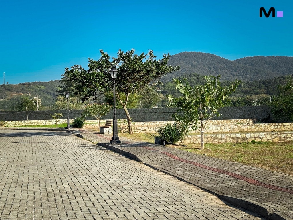 Rua de paralelepípedos no Condomínio Vale das Pedras com montanhas ao fundo.