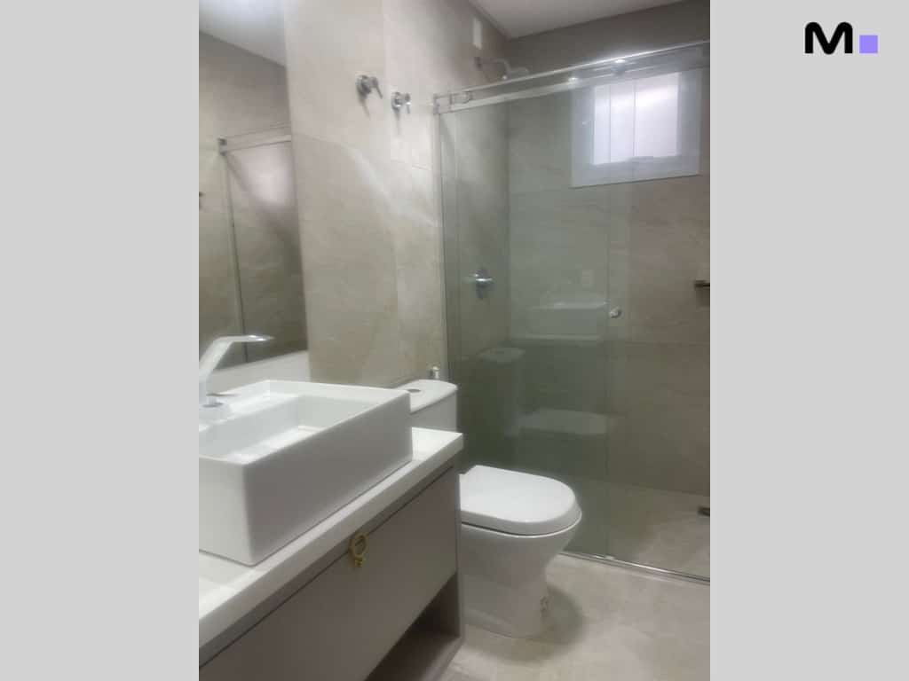 Banheiro moderno com pia branca, vaso sanitário e box de vidro no Condomínio House Haras.