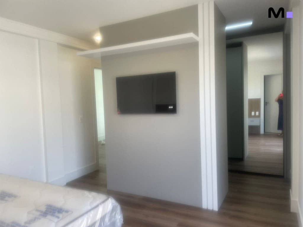 Quarto moderno com TV e espelho no Condomínio House Haras. Design clean e iluminação suave.