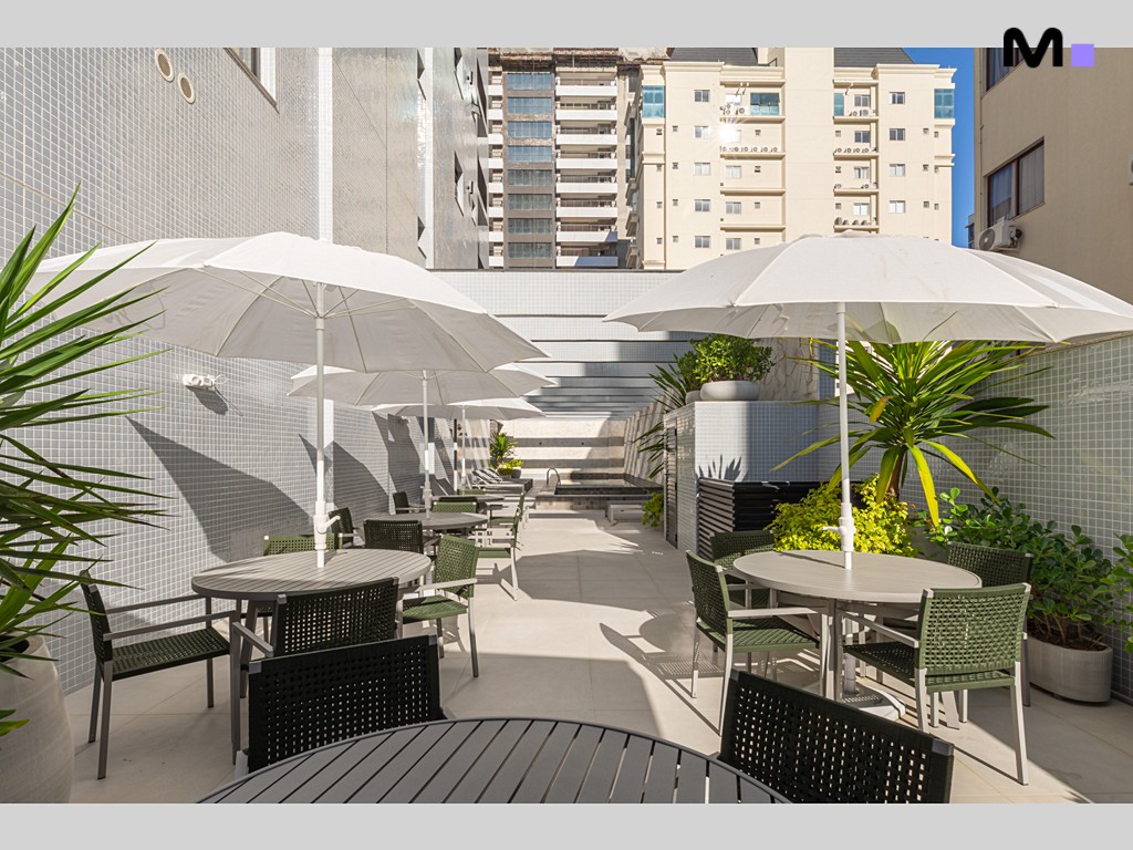 Terraço do Vila Aurora Residence com mesas, cadeiras e guarda-sóis, criando um ambiente relaxante.