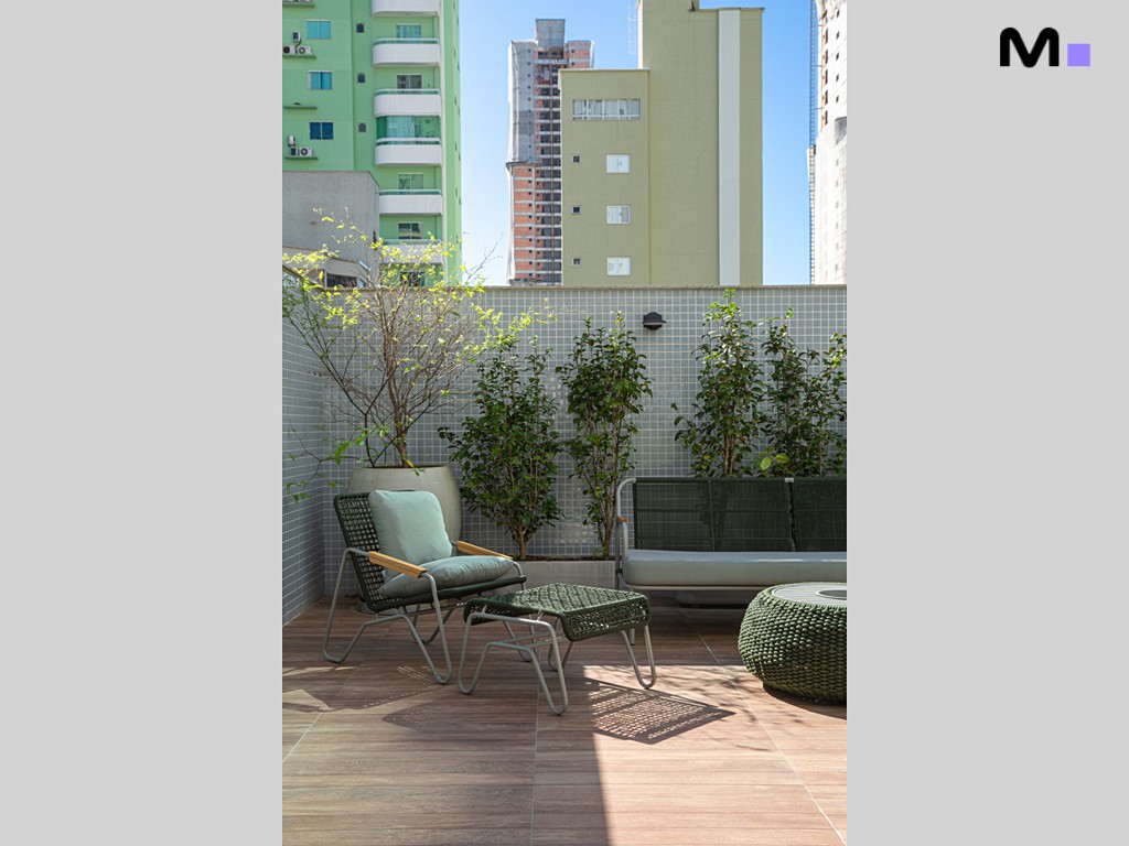 Varanda da Vila Aurora Residence com móveis de vime, plantas e vista urbana.