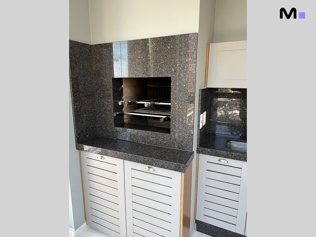 Churrasqueira moderna em granito preto com armários brancos, parte da Realta Residence.