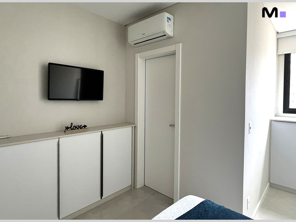 Quarto moderno no Realta Residence: TV, armário branco e ar condicionado.