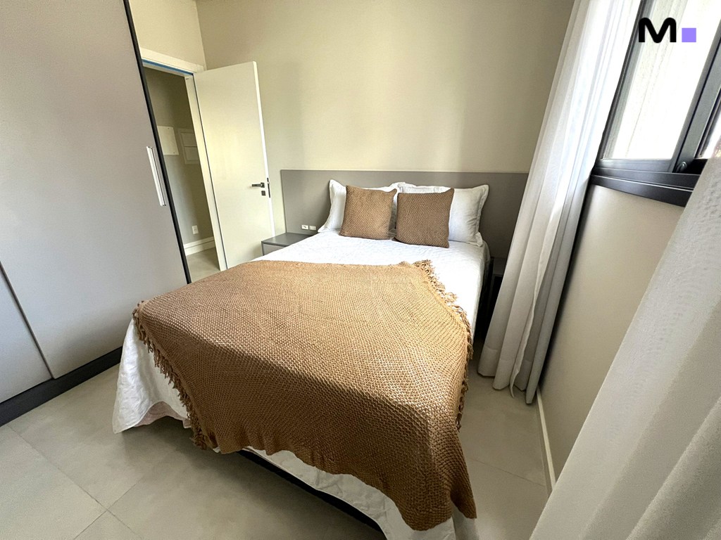 Quarto moderno e iluminado no Realta Residence, com cama de casal, armário e janela com cortina branca.