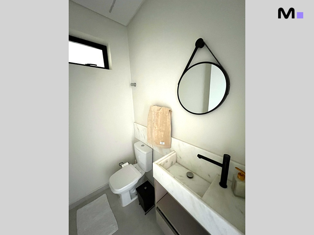 Banheiro moderno com pia de mármore, espelho redondo e vaso sanitário branco. Realta Residence.