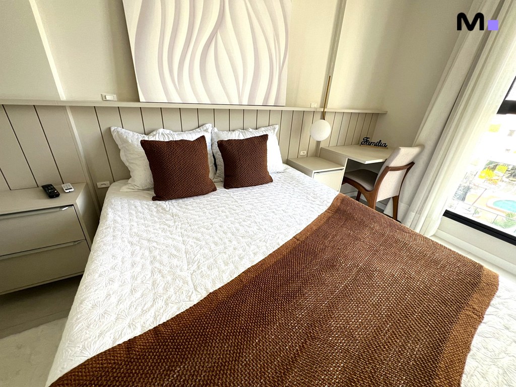 Quarto acolhedor no Realta Residence com cama, roupa de cama branca e detalhes em marrom.