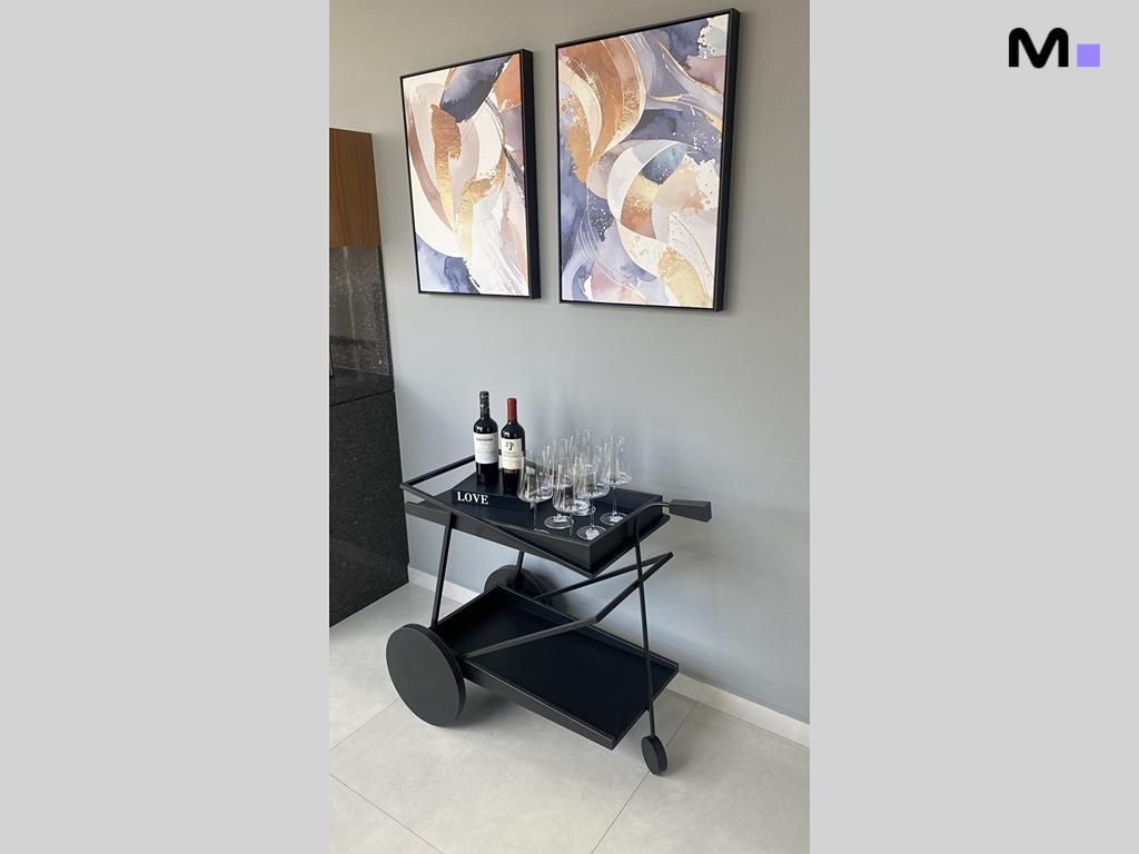 Carrinho de bar preto com vinhos e taças sob quadros abstratos na Realta Residence.